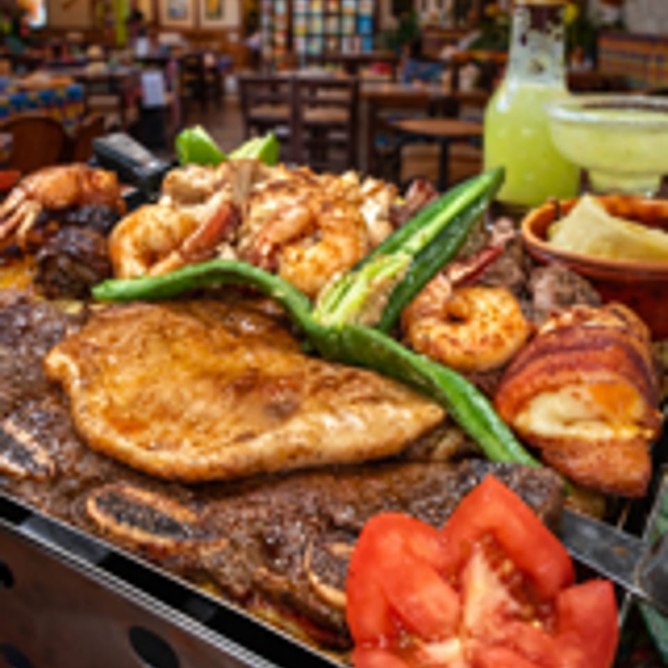 Grilled meats and shrimp fajitas with a tomato slice, in a vibrant Mexican restaurant setting.