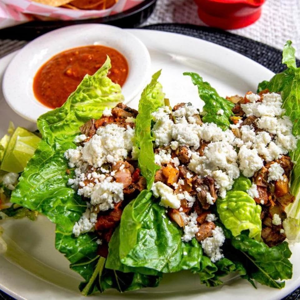 Lettuce wraps filled with meat and crumbled white cheese, served with lime wedges and salsa.