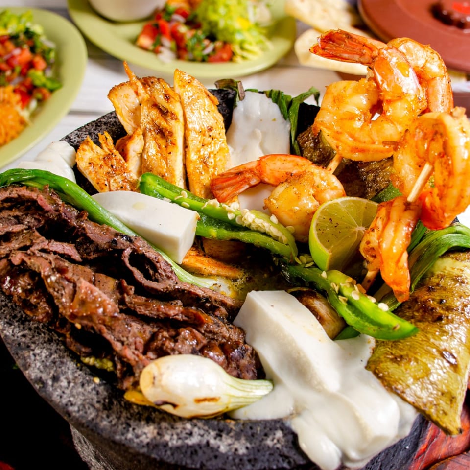 A molcajete filled with grilled chicken, shrimp, steak, peppers, onions, and cheese.